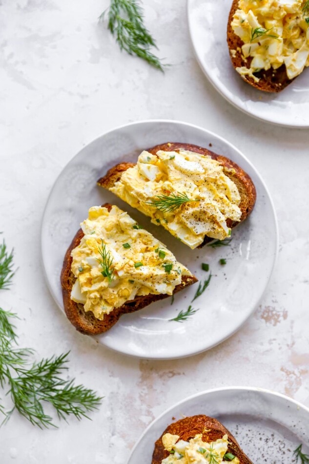 A plate with a slice of bread topped with healthy egg salad. The slice has been cut in half.