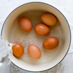 Six eggs in a saucepan. Water is being poured onto the eggs.