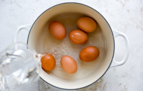 Six eggs in a saucepan. Water is being poured onto the eggs.