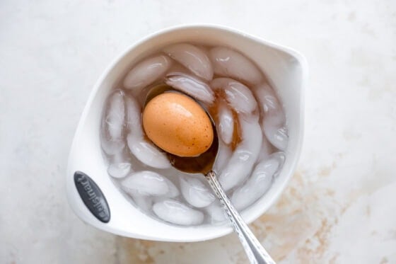 Removing a hard boiled egg from an ice bath with a spoon.