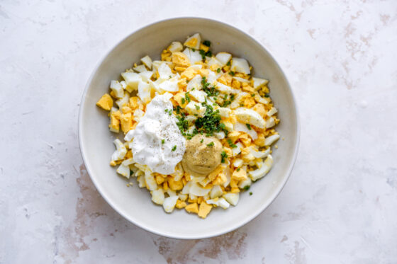 Hard boiled egg pieces, greek yogurt, dijon mustard, chives, pepper and salt in a mixing bowl.