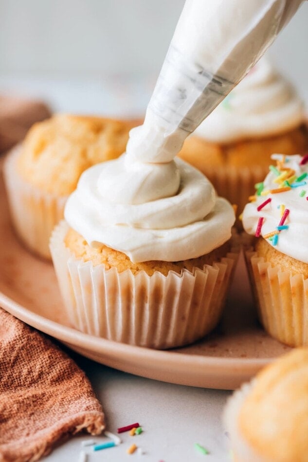 A healthy vanilla cupcake being topped with vanilla icing.