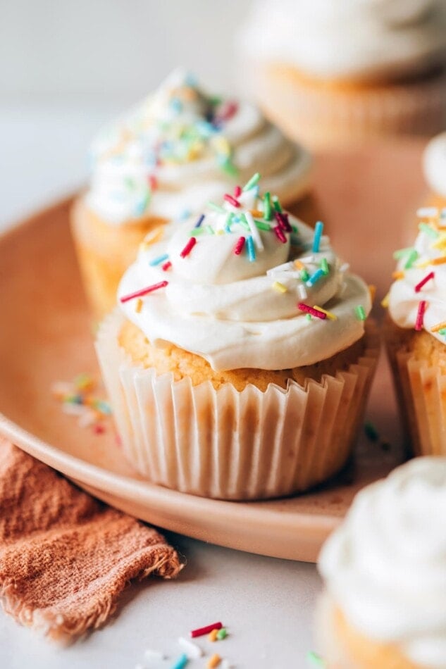 A healthy vanilla cupcake in a paper liner topped with vanilla icing and sprinkles.