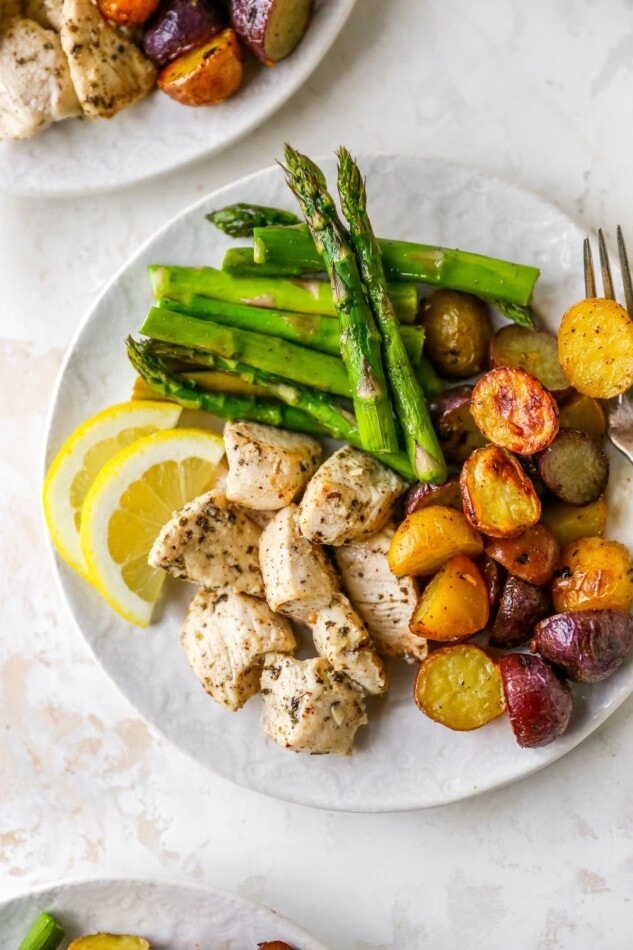 A plate with asparagus, chicken, potatoes and lemon wedges.