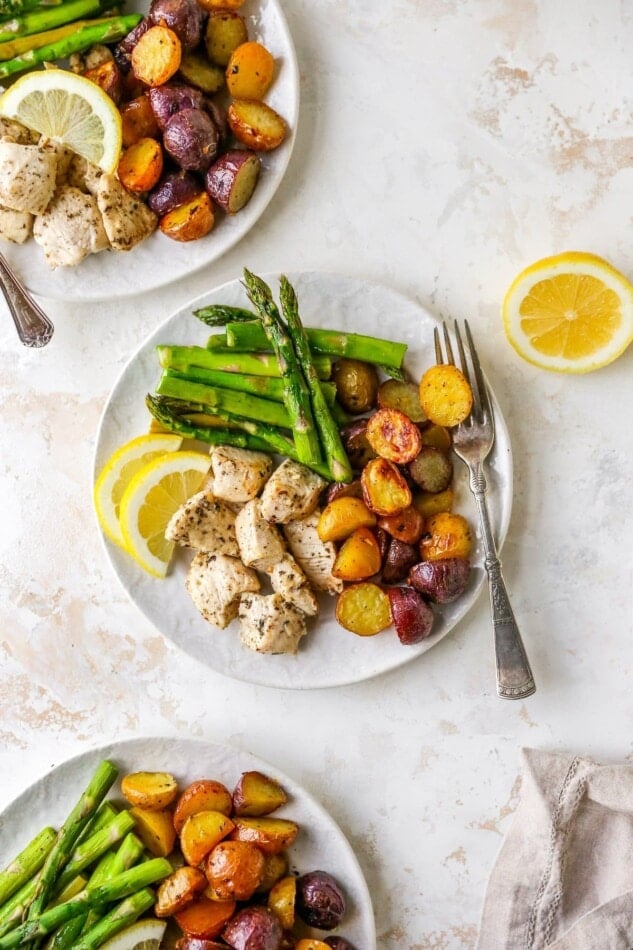 A plate with asparagus, chicken, potatoes and lemon wedges. Two other plates are around the centered plate.