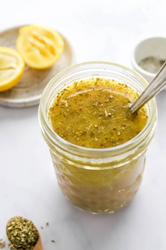 A jar with lemon vinaigrette. A spoon sticks out of the jar.