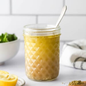 A jar with lemon vinaigrette. A spoon sticks out of the top of the jar.