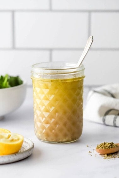 A jar with lemon vinaigrette. A spoon sticks out of the top of the jar.