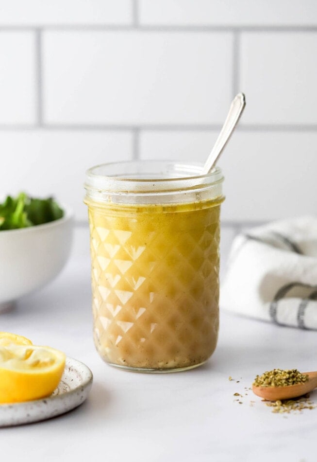 A jar with lemon vinaigrette. A spoon sticks out of the top of the jar.