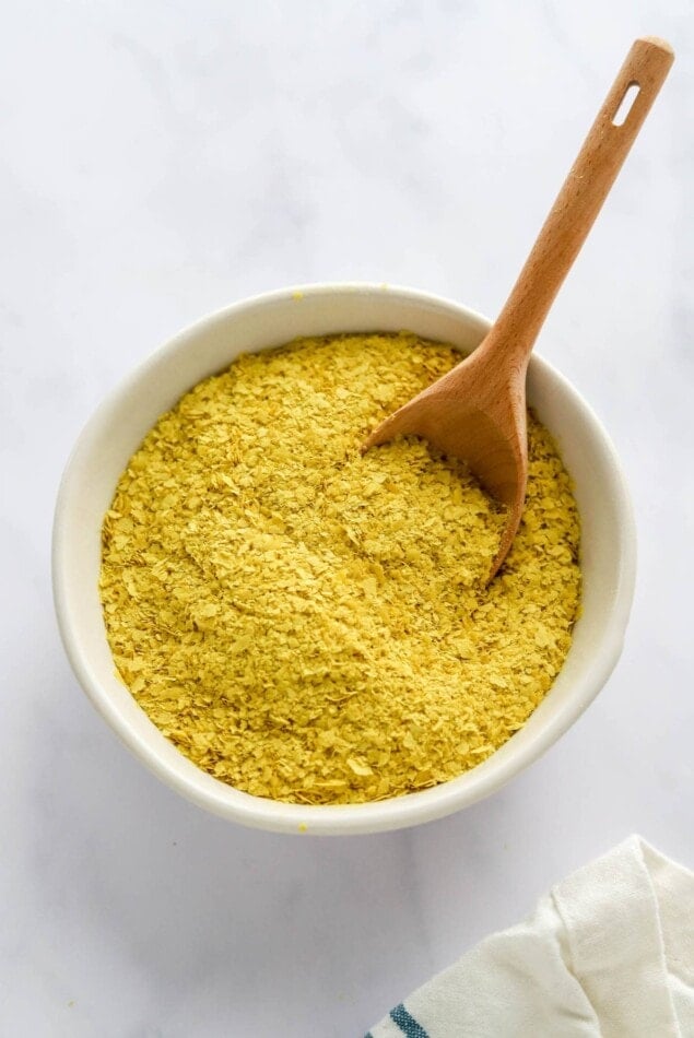 A bowl containing nutritional yeast. A small wooden spoon rests in the bowl.