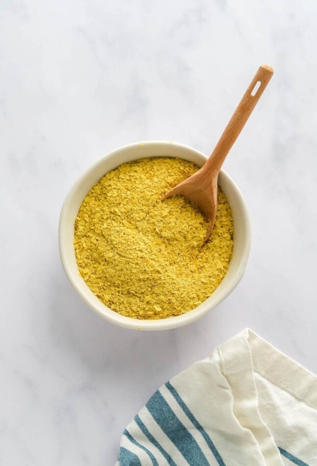 A bowl containing nutritional yeast. A small wooden spoon rests in the bowl.