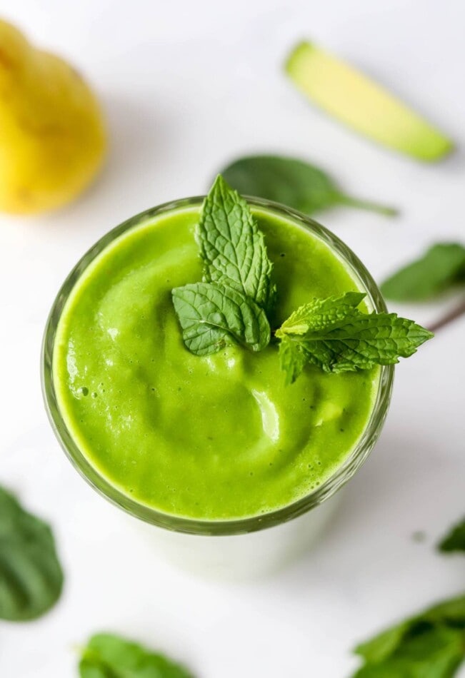 An overhead view of a drinking glass containing pear smoothie topped with fresh mint leaves.