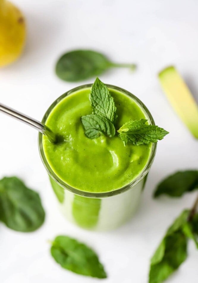 An overhead view of a drinking glass containing pear smoothie topped with fresh mint leaves. A straw sticks out of the glass.