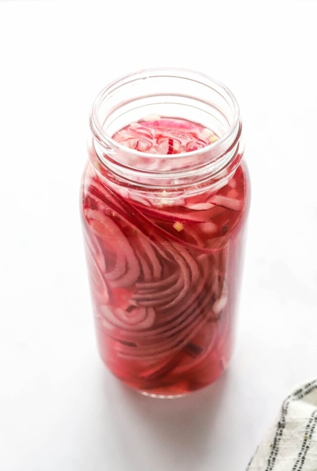 A tall, slender jar containing quick pickled onions.