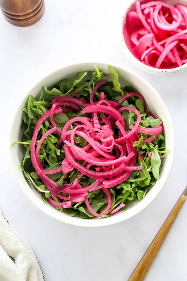 Salad greens in a bowl topped with quick pickled onions.