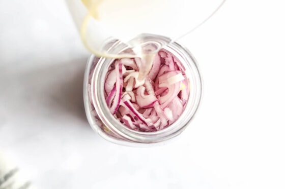 Pouring the vinegar mixture into the jar of onions.