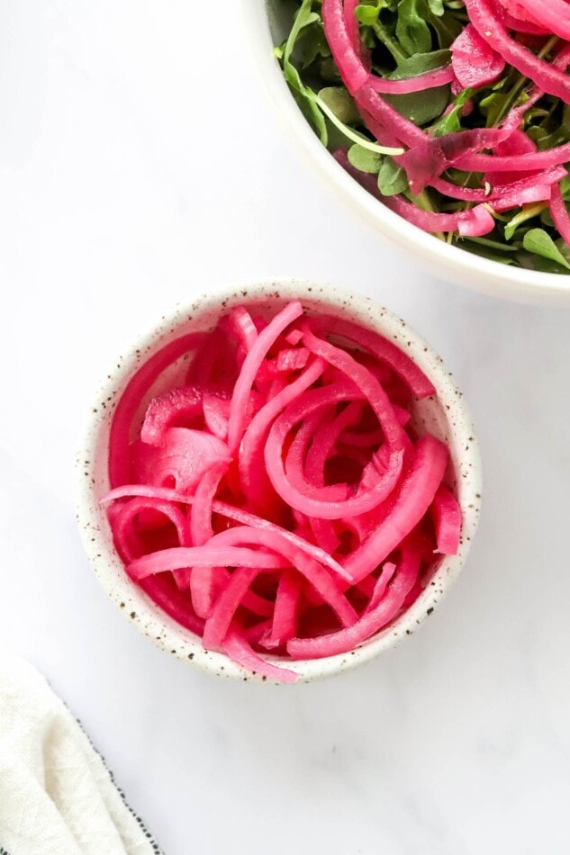 A small bowl of quick pickled onions on the side of a salad bowl topped with quick pickled onions.
