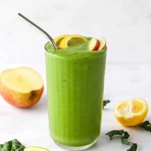 A drinking glass filled with recovery smoothie, topped with lemon and apple wedges. A metal straw sticks out of the top.