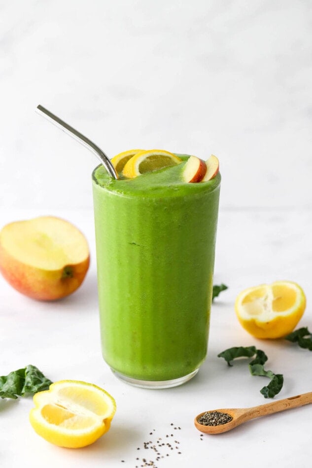 A drinking glass filled with recovery smoothie, topped with lemon and apple wedges. A metal straw sticks out of the top.