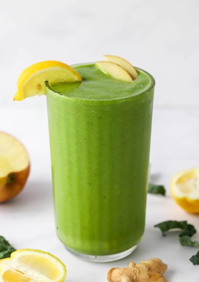 A drinking glass with recovery smoothie topped with lemon and apple wedges.