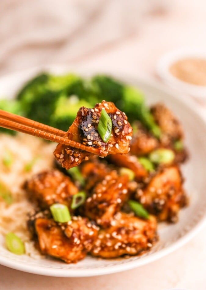 Chopsticks holding up a piece of sesame chicken.