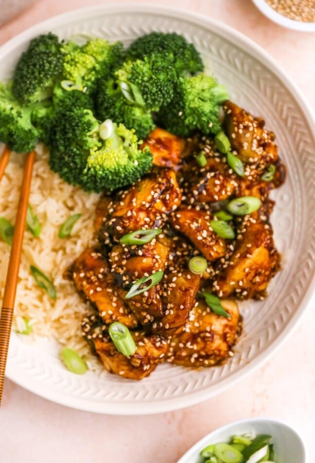 An overhead closeup view of sesame chicken on a plate. Rice and broccoli are also on the plate.