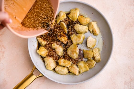 Pouring the sesame sauce onto the chicken in a pan.