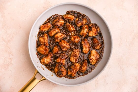 Sesame chicken cooking in sauce in a pan.