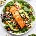 A plate of superfood salad topped with a filet of salmon topped with quick pickled onions, sweet potato croutons and a lemon vinaigrette.