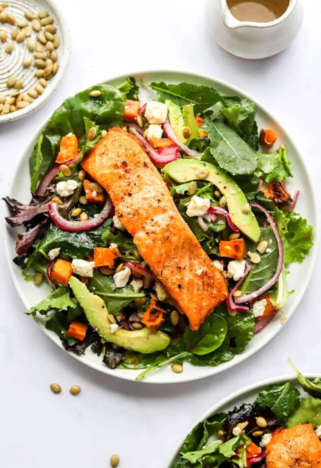 A plate of superfood salad topped with a filet of salmon topped with quick pickled onions, sweet potato croutons and a lemon vinaigrette.