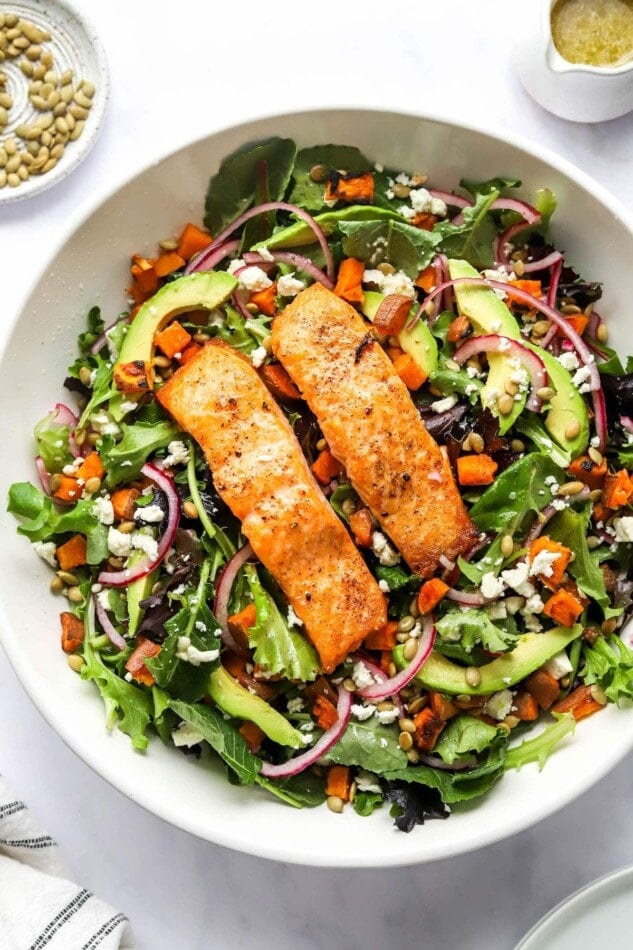 A serving bowl of superfood salad topped with salmon filet.