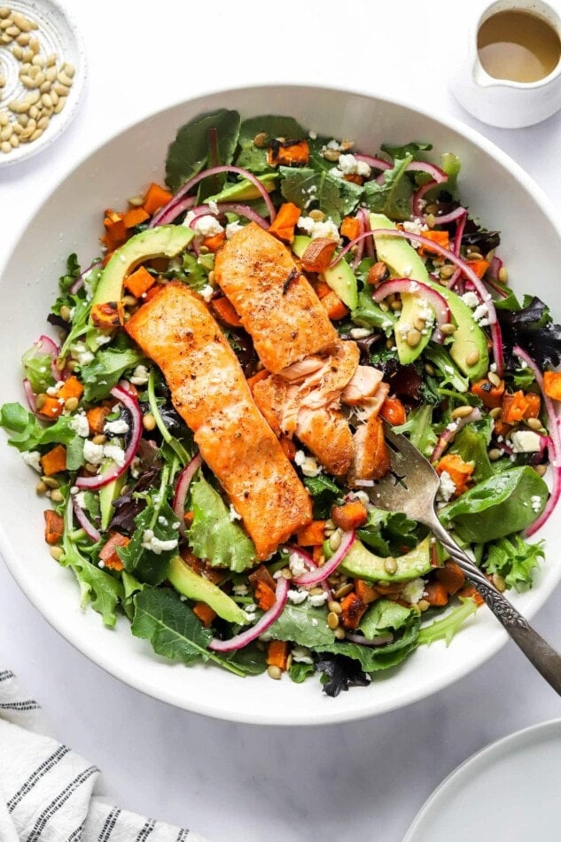 A serving bowl of superfood salad topped with salmon filet.