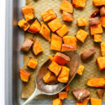 A sheet pan of sweet potato croutons, a serving spoon is resting on the sheet pan with some croutons on it.