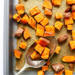 A sheet pan of sweet potato croutons, a serving spoon is resting on the sheet pan with some croutons on it.