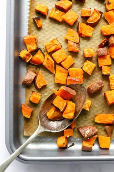 A sheet pan of sweet potato croutons, a serving spoon is resting on the sheet pan with some croutons on it.