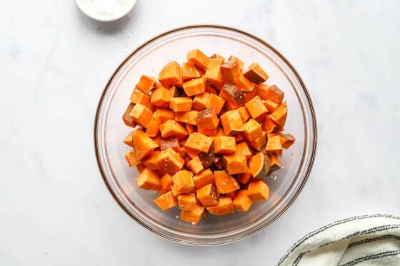 Chopped sweet potato in a bowl tossed with salt and olive oil.