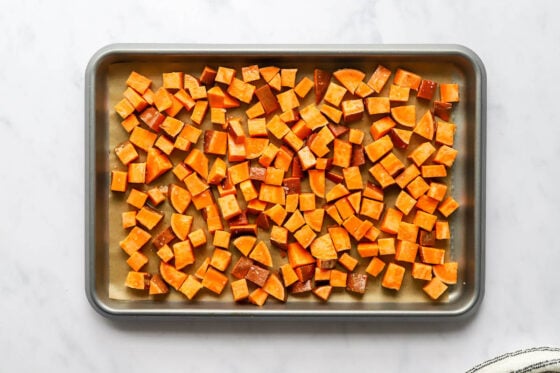 Sweet potato chunks spread across a baking sheet lined in parchment paper.