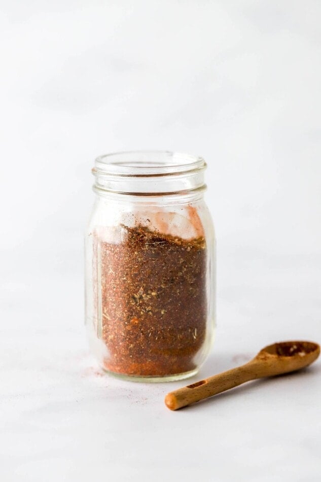 Taco seasoning in a small spice jar. A wooden spoon lays next to the jar.