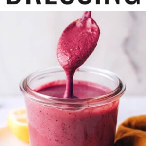 A small jar containing blueberry tahini dressing. A spoon is dripping the dressing back into the jar.