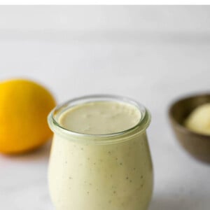 A small tulip jar containing caesar salad dressing. A small spoon rests next to the jar.