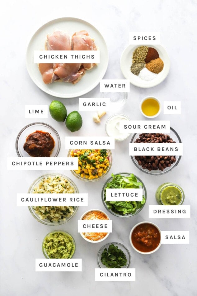 Ingredients measured out to make chicken burrito bowls: chicken thighs, spices, water, garlic, lime, oil, sour cream, corn salsa, black beans, chipotle peppers, lettuce, cauliflower rice, dressing, cheese, salsa, cilantro and guacamole.