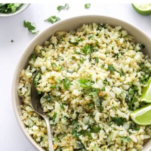 A closeup of a serving bowl containing cilantro lime cauliflower rice. A spoon rests in the bowl.