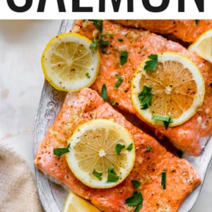 Close up of salmon filets on a platter, topped with lemon slices and parsley.