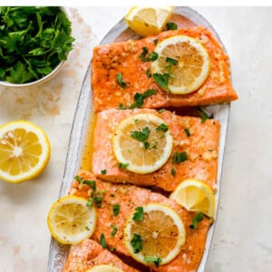 Platter of four salmon filets topped with lemon slices and parsley.