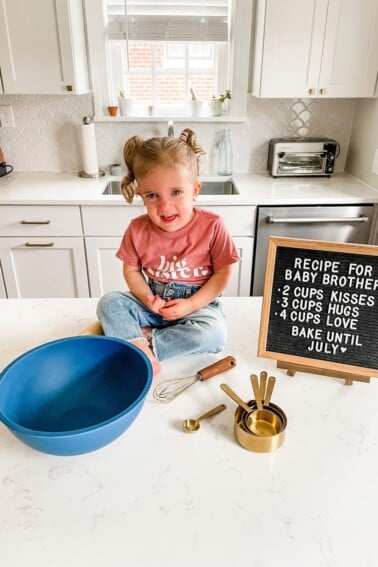 Toddler girl in a big sister shirt with recipe for baby brother sign.