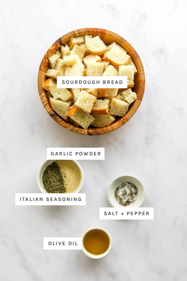 Ingredients measured out to make sourdough croutons: sourdough bread, garlic powder, Italian seasoning, salt, pepper and olive oil.
