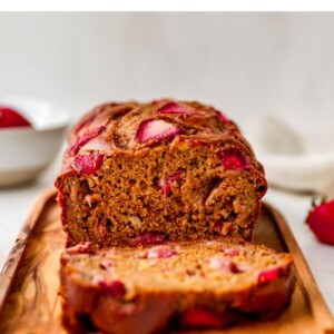 A loaf of strawberry banana bread, a slice has been cut and is resting next to the loaf.