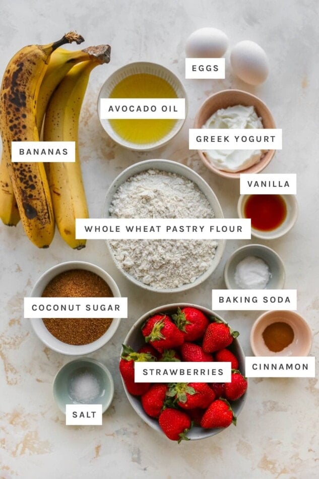 Ingredients measured out to make strawberry banana bread: bananas, avocado oil, eggs, Greek yogurt, vanilla, whole wheat pastry flour, baking soda, coconut sugar, strawberries, cinnamon and salt.