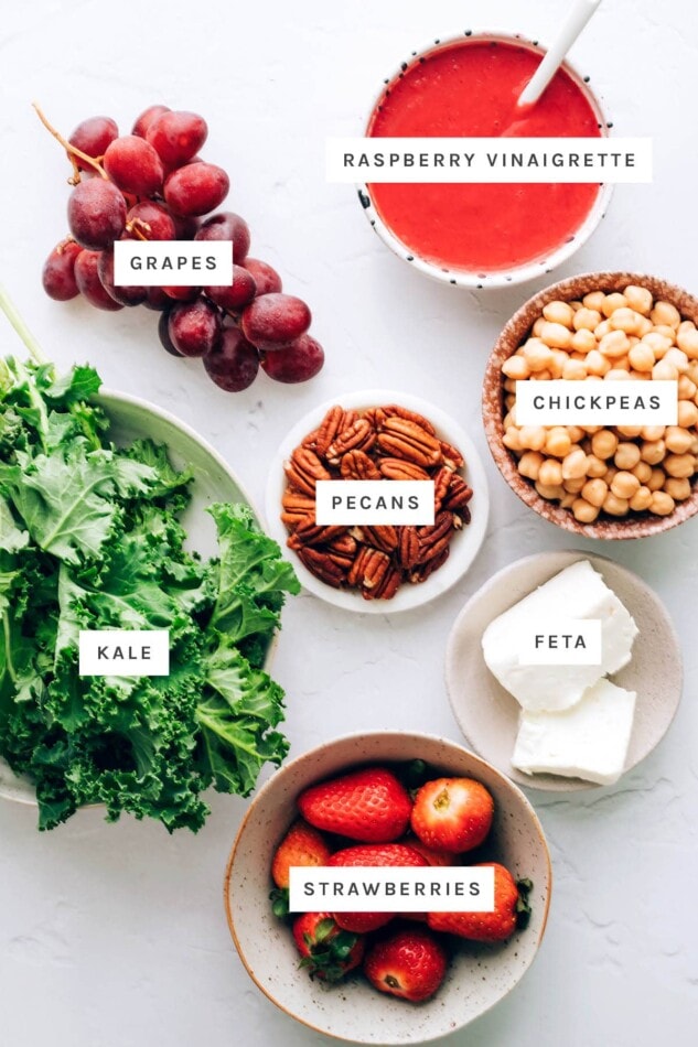 Ingredients measured out to make strawberry kale salad: grapes, raspberry vinaigrette, chickpeas, pecans, feta, kale, strawberries.