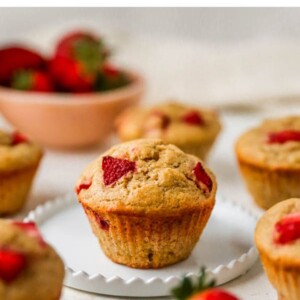 A muffin resting on a plate. The plate is surrounded by other muffins.